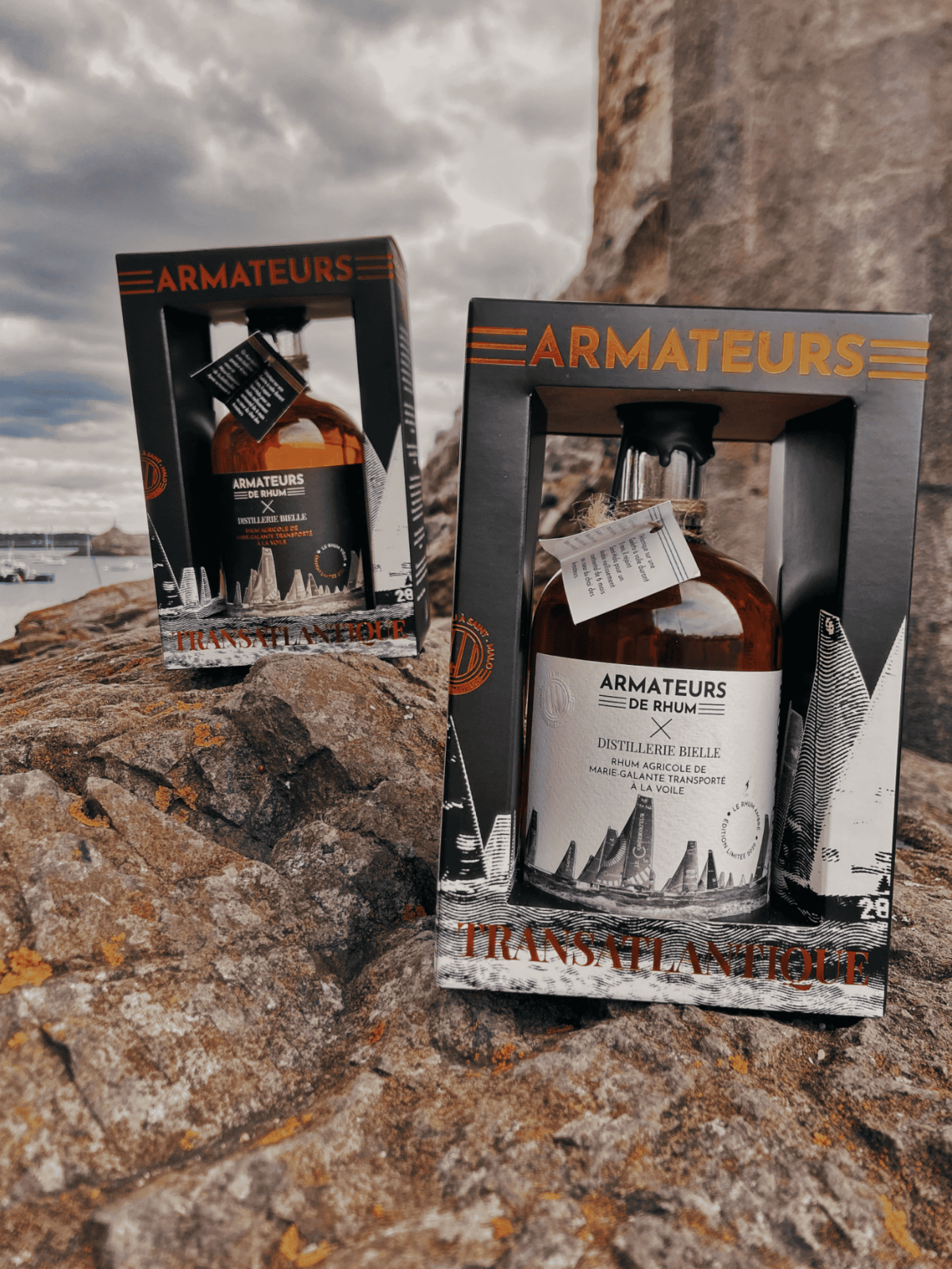 Coffret Rhum Armateurs présenté sur rocher au bord de mer – rhum breton artisanal.